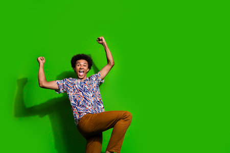 Photo of lucky excited man dressed print shirt rising fists shouting yeah empty space isolated green...