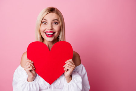 Photo of excited funky lady wear off shoulders dress smiling rising red heart empty space isolated pink color backgroundの写真素材
