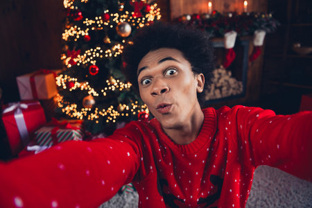 Photo of childish impressed guy dressed red ugly x-mas pullover big eyes recording new year video greetings indoors house roomの写真素材