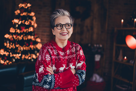 Photo of cheerful thoughtful lady dressed red print x-mas pullover spectacles arms folded enjoying new year spirit indoors house roomの写真素材