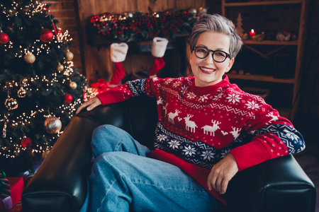 Photo of sweet adorable lady dressed red print x-mas pullover spectacles relaxing arm chair enjoying new year indoors house roomの写真素材