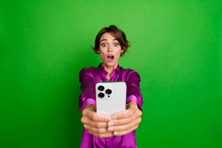 Photo of excited glamour girl open mouth hold a smartphone wow win jackpot esport bet isolated on green color backgroundの写真素材