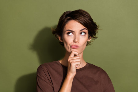 Portrait of minded confused woman with short hair wear oversize t-shirt gloomy look empty space isolated on green color backgroundの写真素材