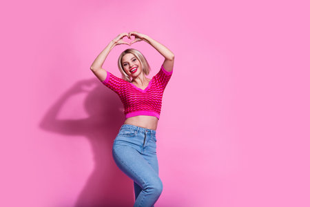 Photo of nice positive woman with bob hairdo wear stylish clothes denim pants fingers showing heart over head isolated on pink backgroundの写真素材