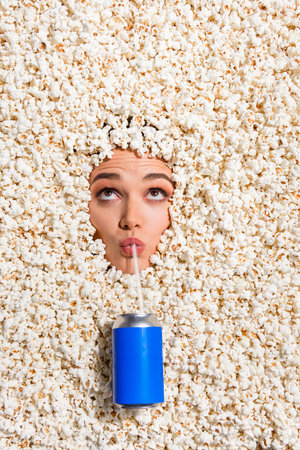 Vertical top view portrait of funky girl straw sipping soda drink can look up empty space face inside popcorn backgroundの写真素材