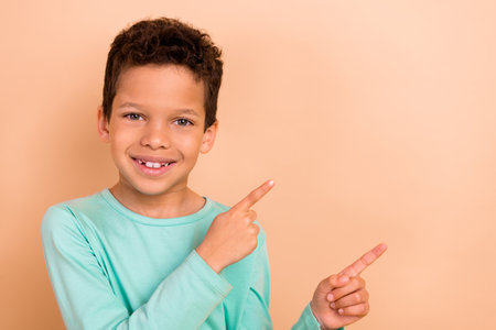 Photo of cheerful nice cute boy wear stylish turquoise clothes introduces news logo brand empty space isolated on beige color backgroundの写真素材