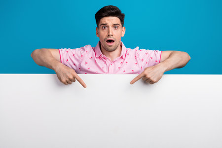 Portrait of impressed speechless man open mouth direct fingers empty space banner isolated on blue color backgroundの写真素材