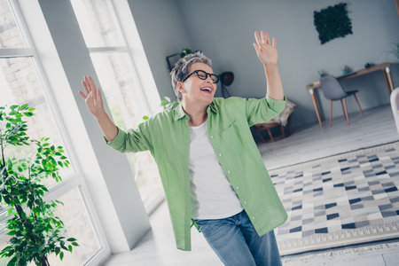 Photo of carefree laughing funky lady mature age raised palms up enjoying weekend atmosphere in living room bought new apartment todayの写真素材