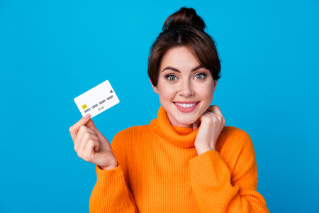 Photo of cheerful tricky lady wear knitted pullover rising bank card isolated blue color backgroundの写真素材