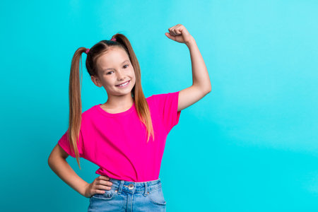 Photo of glad adorable cute girl wear stylish pink clothes showing muscular arm empty space isolated on cyan color backgroundの写真素材