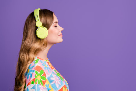 Portrait of satisfied positive girl with curly hairdo in bluetooth headphones enjoy sound quality isolated on violet color backgroundの写真素材
