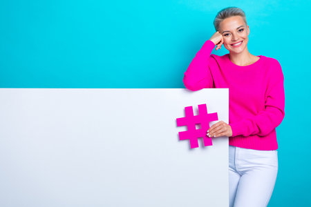 Photo of lovely woman with short hair dressed jumper lean on white poster empty space hold hashteg isolated on teal color backgroundの写真素材
