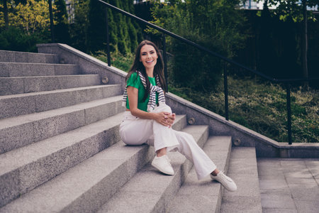 Photo of cheerful glad lovely woman dressed stylish clothes sitting on stairs in park spending summer days outdoorsの写真素材