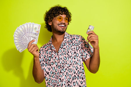 Photo portrait of nice young male hold money usd roll wear trendy pink leopard print garment isolated on yellow color backgroundの写真素材