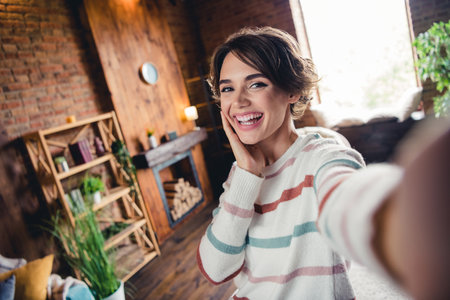 Portrait of positive lovely lady make selfie arm touch cheek beaming smile spend free time loft flat insideの写真素材