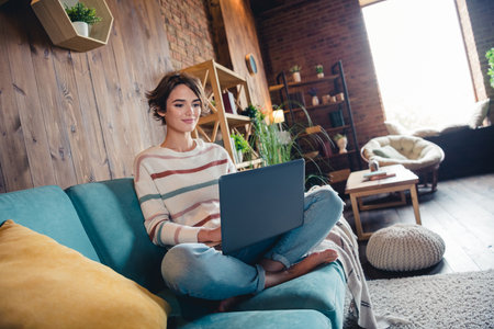 Full size photo of nice positive girl sit barefoot comfy sofa use wireless netbook networking house insideの写真素材