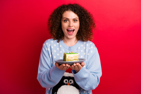 Photo of impressed funky girl dressed ugly christmas sweater preparing delicious cake isolated red...