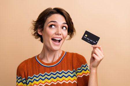 Photo of astonished nice lady open mouth arm hold debit card look empty space isolated on beige color backgroundの写真素材