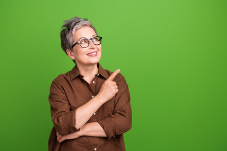 Photo of retired woman with short hair wear brown shirt in glasses look directing at sale empty space isolated on green color backgroundの写真素材