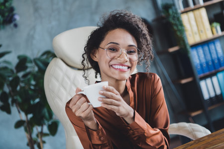 Photo of positive stunning elegant person sit chair toothy smile hands hold fresh coffee mug modern office insideの写真素材