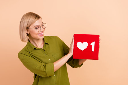 Portrait of cute pleasant girl wear khaki shirt in eyewear look at one social media heart in hands...