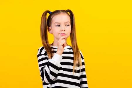Photo of doubtful unsure little child dressed striped pullover arm chin looking empty space isolated yellow color backgroundの写真素材