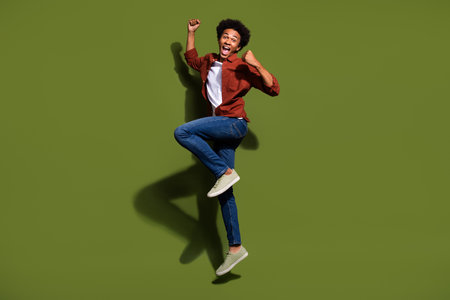 Full body photo of attractive young man jump celebrate winning hooray wear trendy brown clothes isolated on khaki color backgroundの写真素材