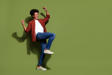 Full length photo of nice young male dancing raise fists achieve goal wear trendy brown garment isolated on khaki color backgroundの写真素材