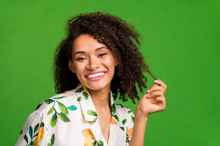 Photo of girly shiny lady wear print shirt smiling holding hair curl empty space isolated green color backgroundの写真素材