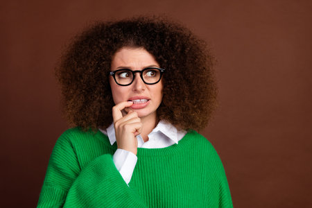 Portrait of minded puzzled person biting finger nail look empty space ponder isolated on brown color backgroundの写真素材