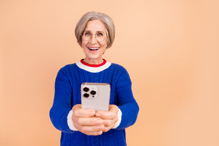 Photo of surprised amazed cheerful woman wear trendy blue clothes using a smartphone isolated on beige color backgroundの写真素材