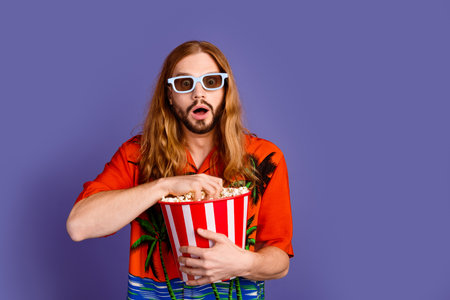 Portrait of astonished crazy guy with red hair in 3d glasses eat popcorn staring at film premiere...