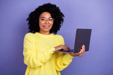 Photo of smart woman with afro hairstyle dressed yellow sweater in eyewear hold laptop write email...