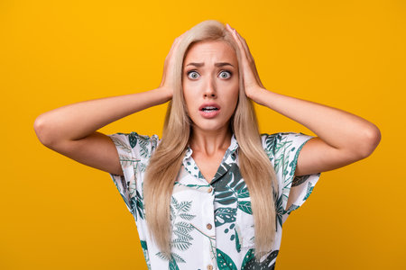Portrait of speechless girl with long hair wear print blouse hold arms on head astonished staring isolated on yellow color backgroundの写真素材