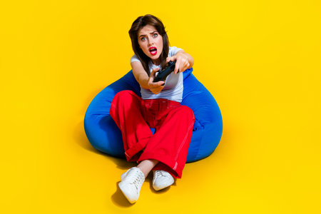 Full length photo of impressed funky woman dressed white t-shirt sitting bean bag loosing game...