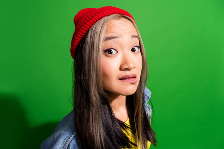 Photo of doubtful unsure lady wear denim jacket biting lip looking you isolated green color backgroundの写真素材