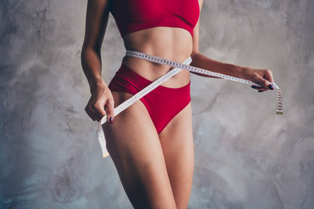 No retouch close up photo of fit gorgeous nice girl wear red panties top measuring waist watch diet isolated on concrete backgroundの写真素材
