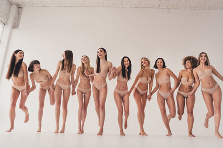 No filter studio photo of pretty excited women wear lingerie fighting women rights holding arms isolated beige color wall backgroundの写真素材