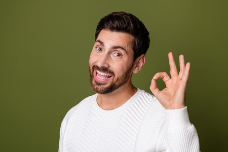 Photo of satisfied cheerful nice man in trendy white sweater showing okey symbol feedback isolated on khaki color backgroundの写真素材