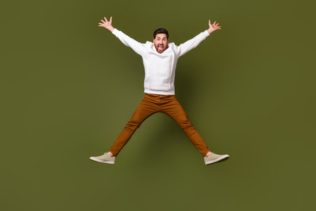Full length photo of overjoyed glad man dressed white clothes flying air raised hands isolated on...