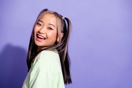 Portrait of good mood pretty girl with ponytails wear oversize pullover stand near logo empty space isolated on violet color backgroundの写真素材