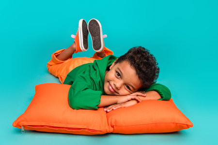 Photo of charming adorable boy dressed stylish green clothes lying comfy soft pillows weekend relax isolated on cyan color backgroundの写真素材