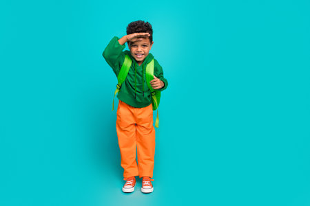 Full length photo of adorable boy wear green clothes hand touch forehead looking far away empty space isolated on cyan color backgroundの写真素材