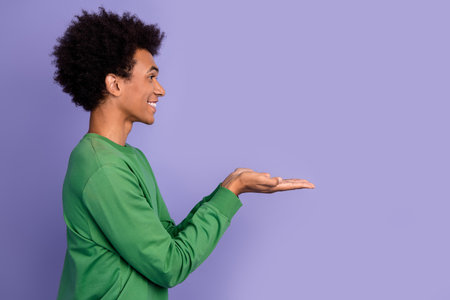 Photo of positive funky guy wear green pullover holding arms empty space isolated purple color backgroundの写真素材