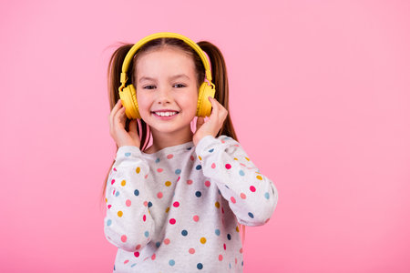 Portrait of good mood schoolgirl with ponytails dressed dotted sleepwear enjoy music in headphones isolated on pink color backgroundの写真素材