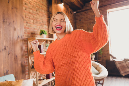 Portrait of delighted ecstatic positive lady closed eyes raise fists accomplishment triumph modern apartment indoorsの写真素材