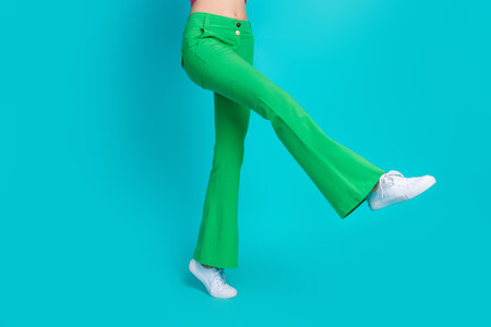 Cropped photo of half body thin funny woman legs dressed green vintage trousers dancing on one leg isolated on blue color backgroundの写真素材