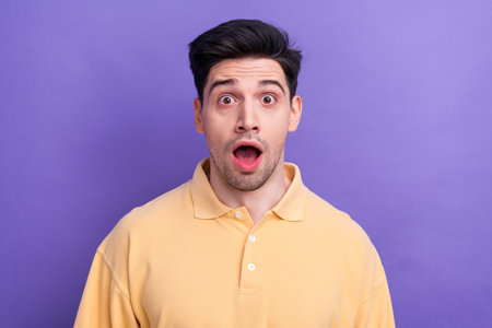 Photo of shocked funky man dressed yellow shirt big eyes open mouth isolated purple color backgroundの写真素材