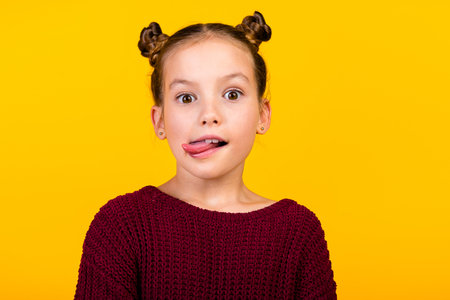 Portrait of positive adorable girl have good mood showing bite tongue empty space isolated on yellow color backgroundの写真素材