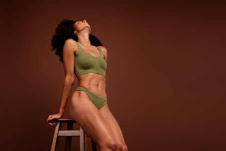 No filter photo of healthy sporty woman flawless muscular body posing stool casual lingerie empty space isolated on brown color backgroundの写真素材